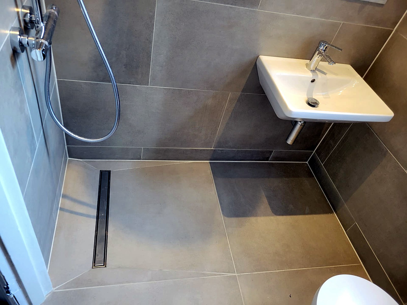 Tiled wet room floor falling to a stainless linear drain beside the wall-hung basin