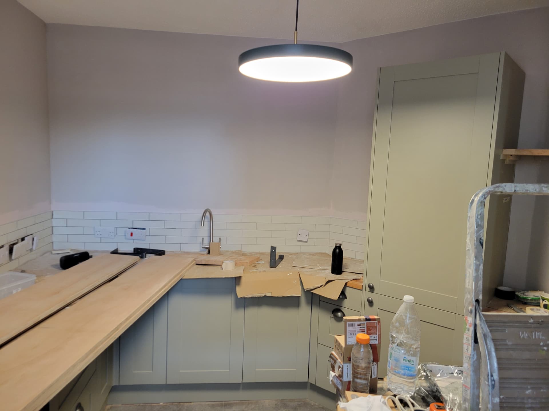 Kitchen during works with new painted cabinets fitted, wall tiling done and timber worktops being installed