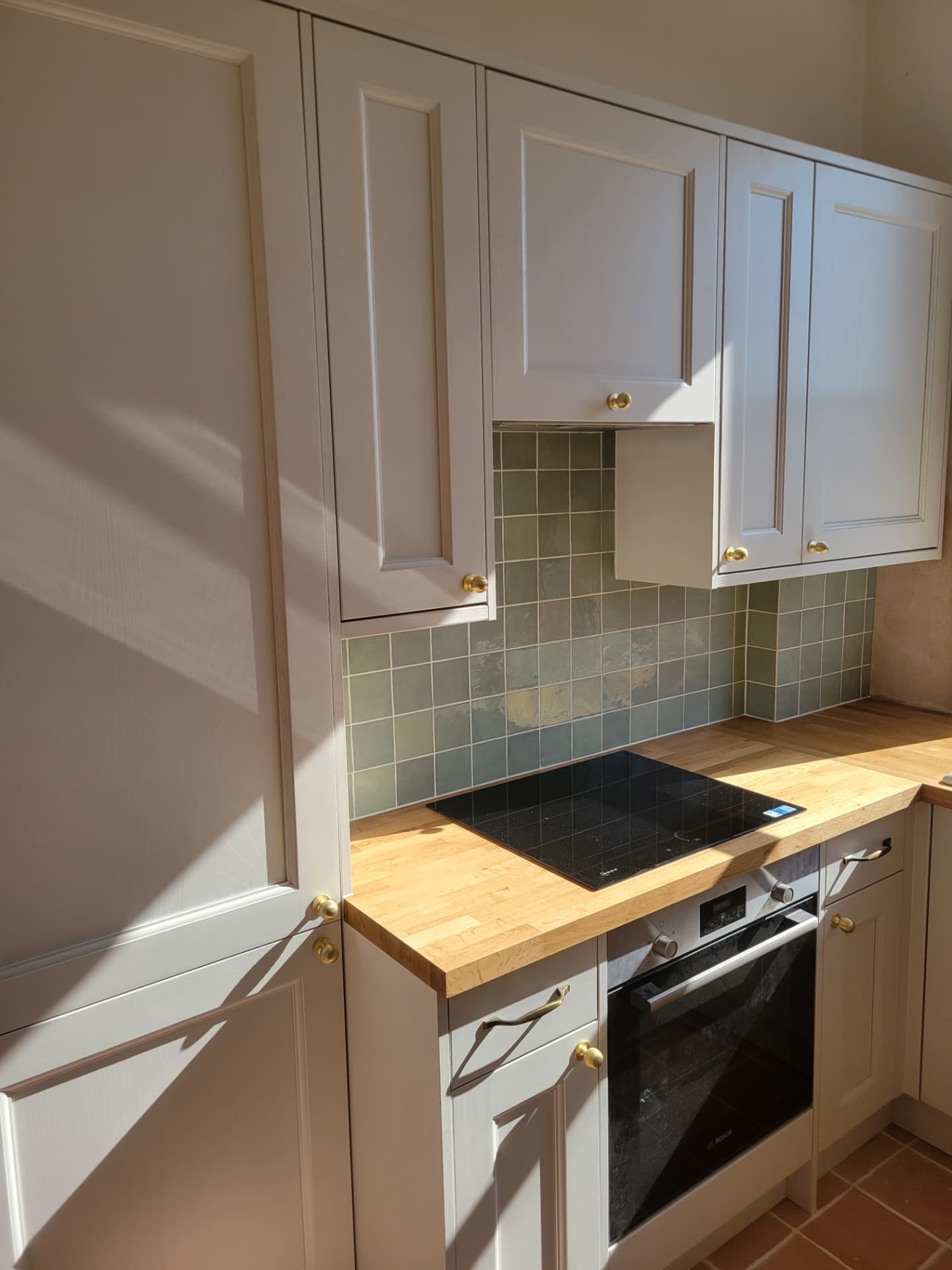 Cabinets, hob and timber worktop beneath the tiled splashback