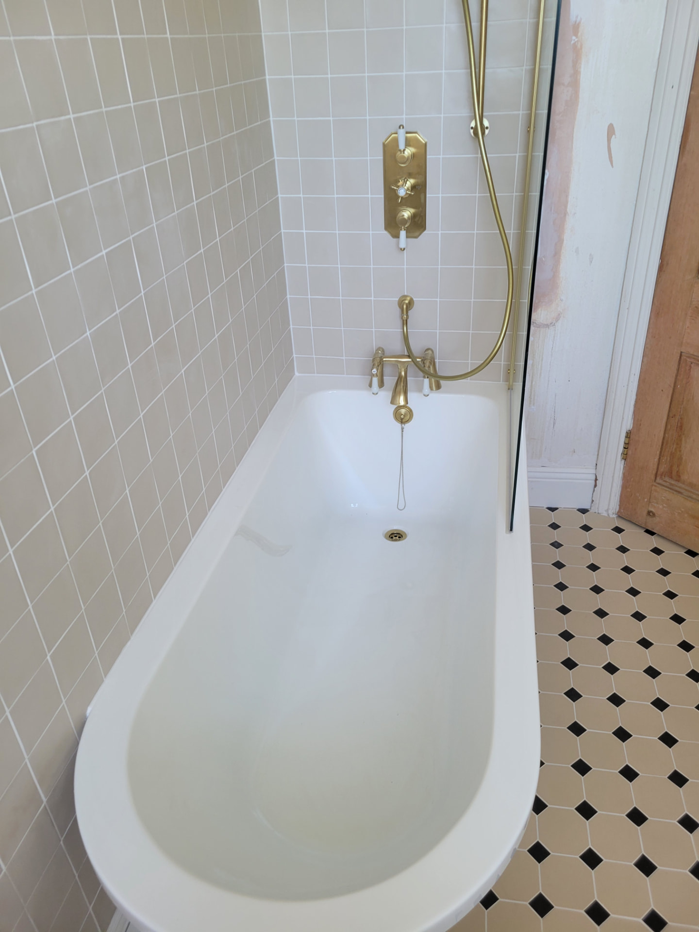 Bath and brass shower fittings against the tiled wall