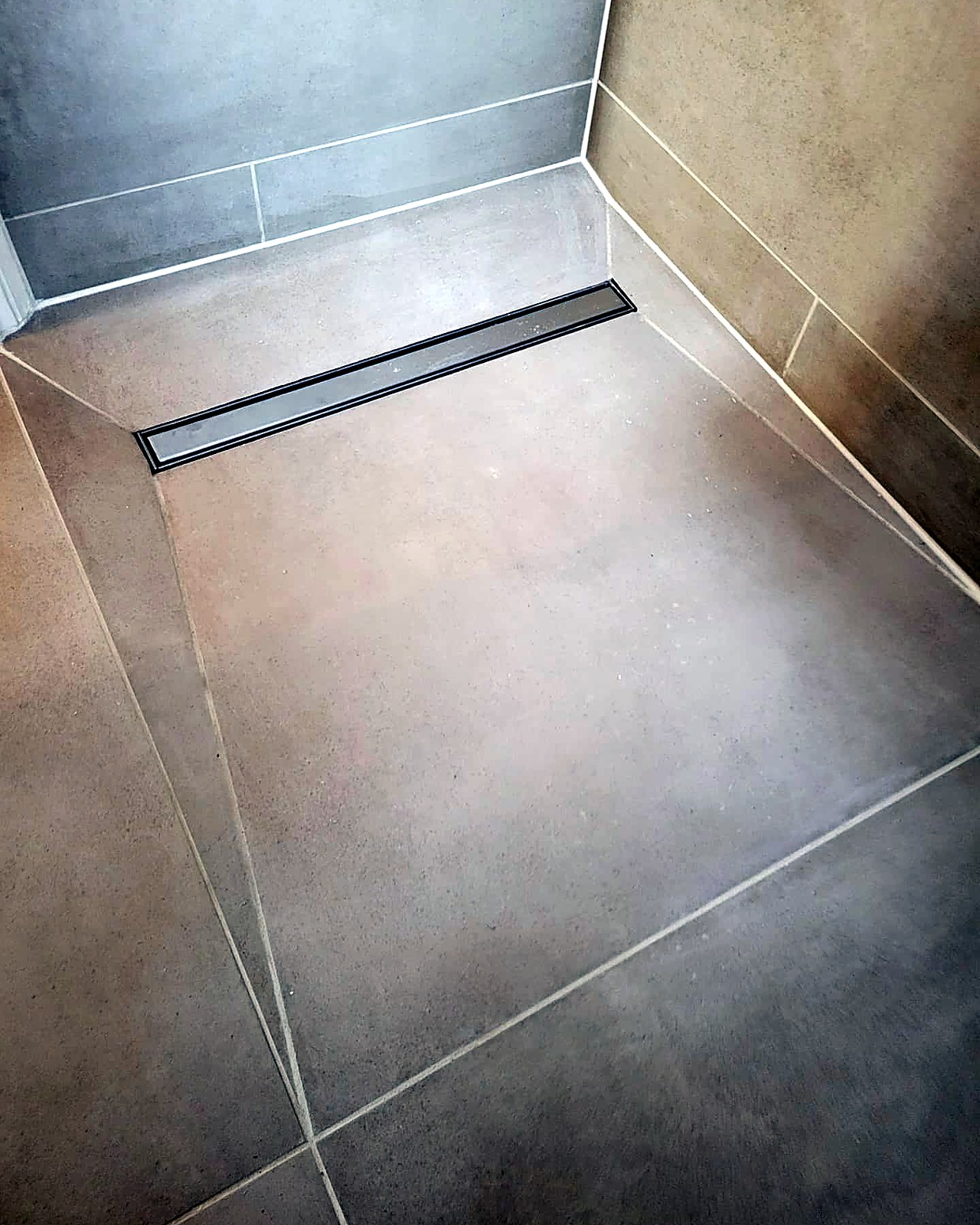 Stainless steel linear drain set flush into the graded porcelain wet room floor