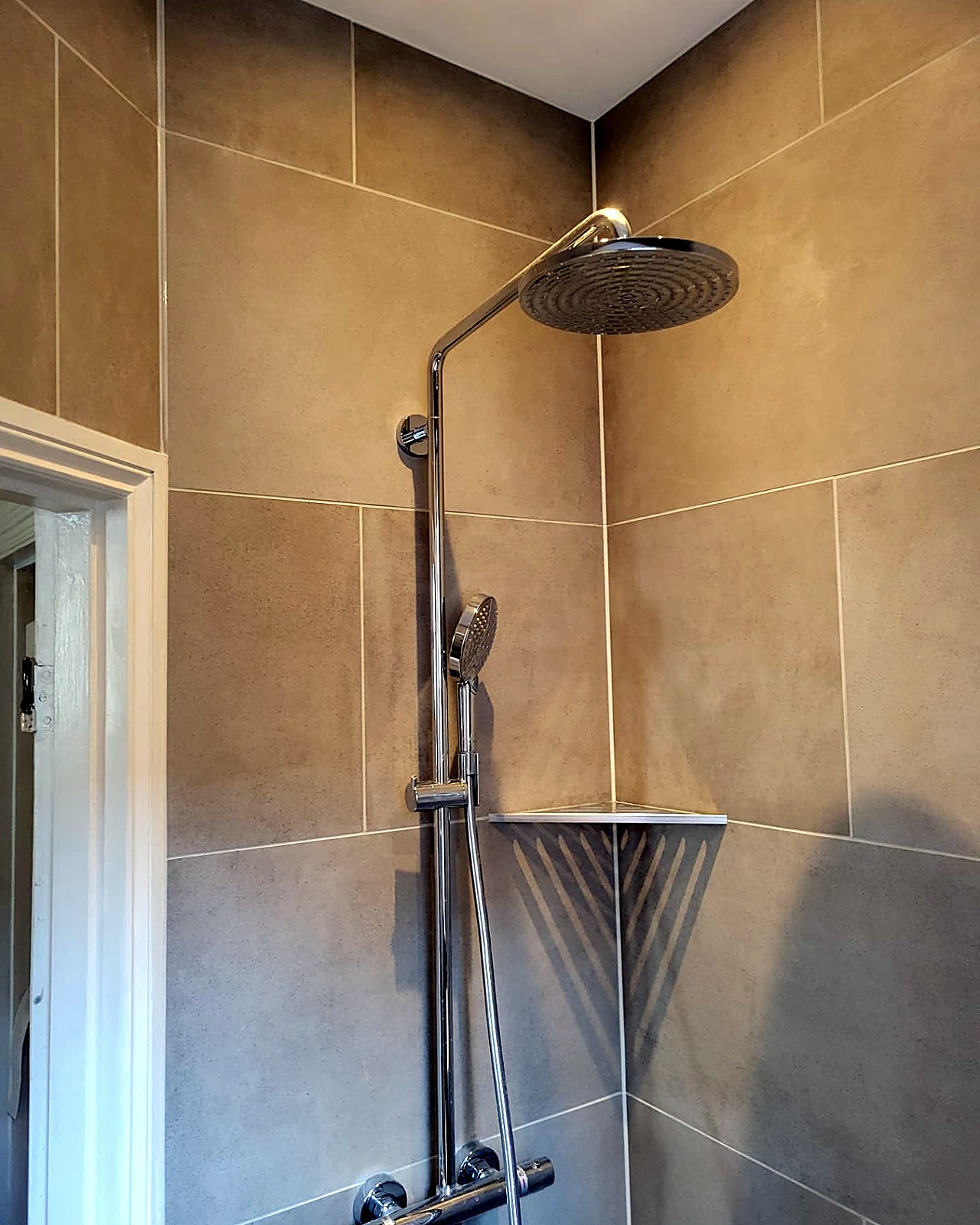 Chrome rainfall shower riser with handset against large-format porcelain tiling