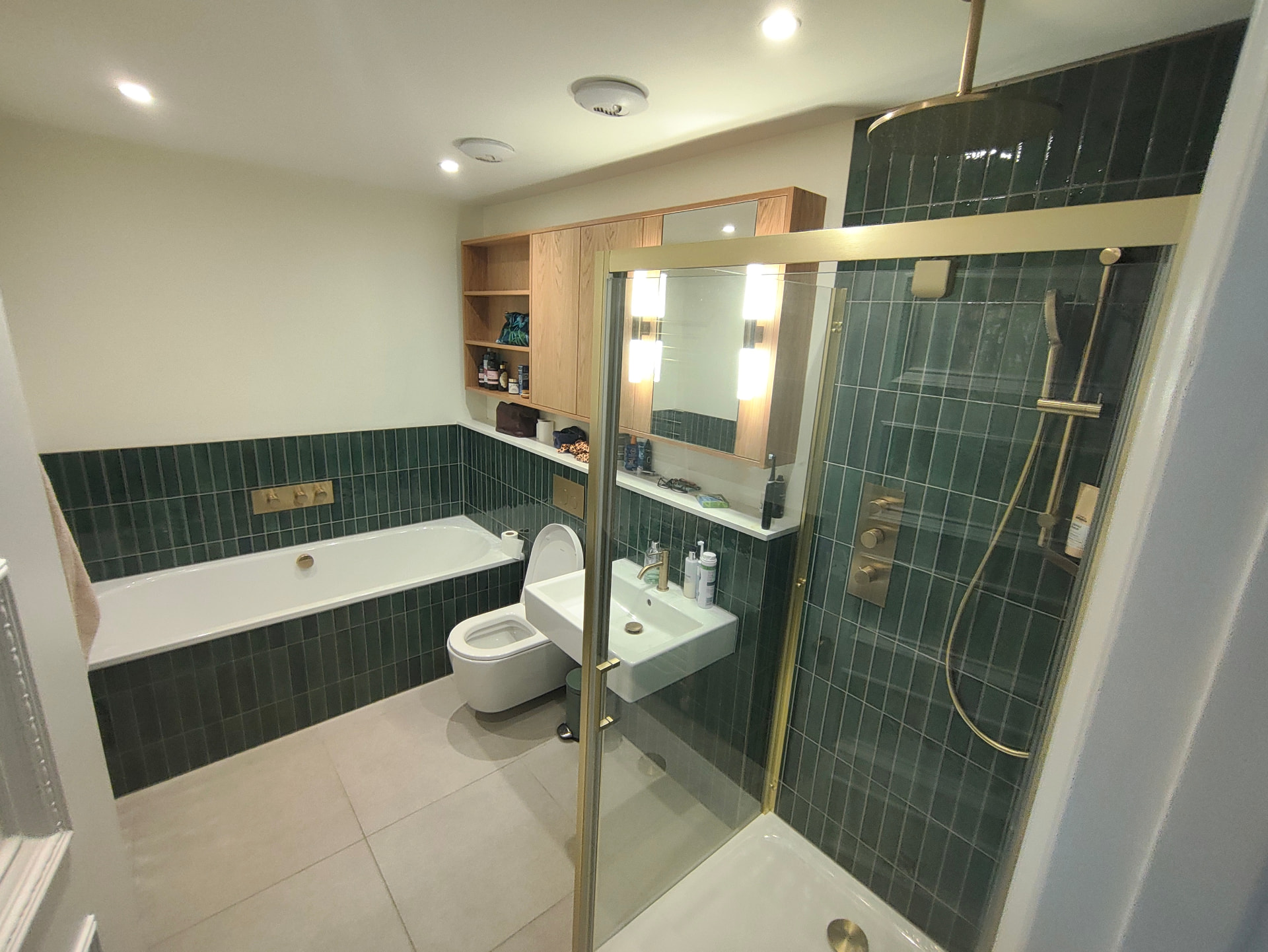 Finished bathroom with deep green vertical tiling, built-in bath, brass fittings and oak cabinetry