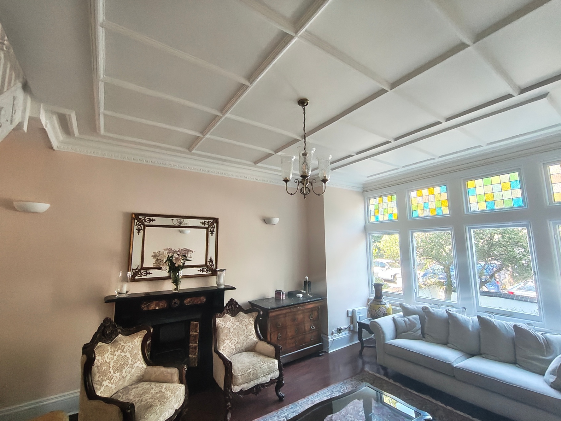 Restored period living room with coffered ceiling, stained glass bay window and original fireplace