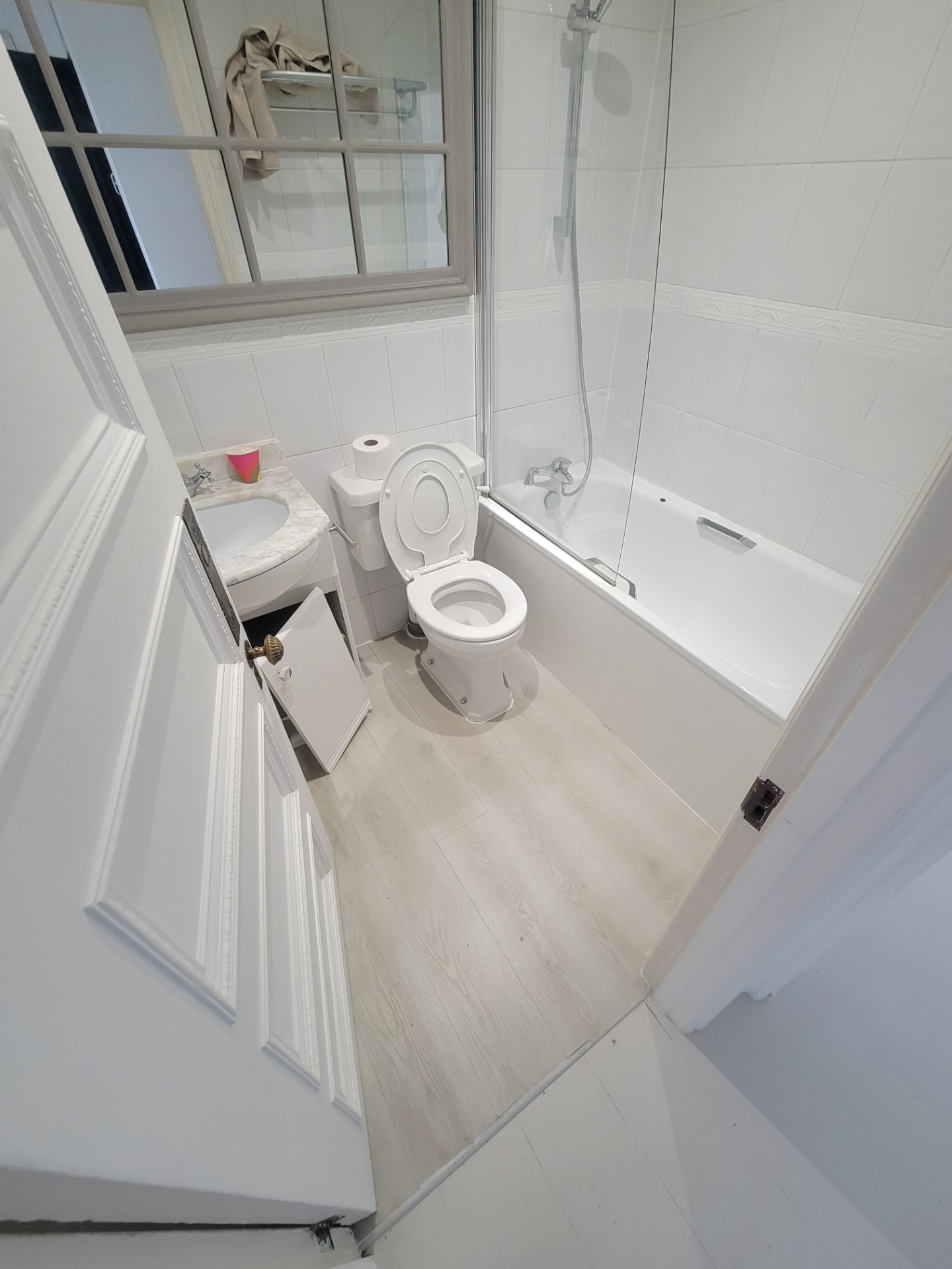 Original bathroom before works with a bath and shower screen, white tiling and laminate flooring