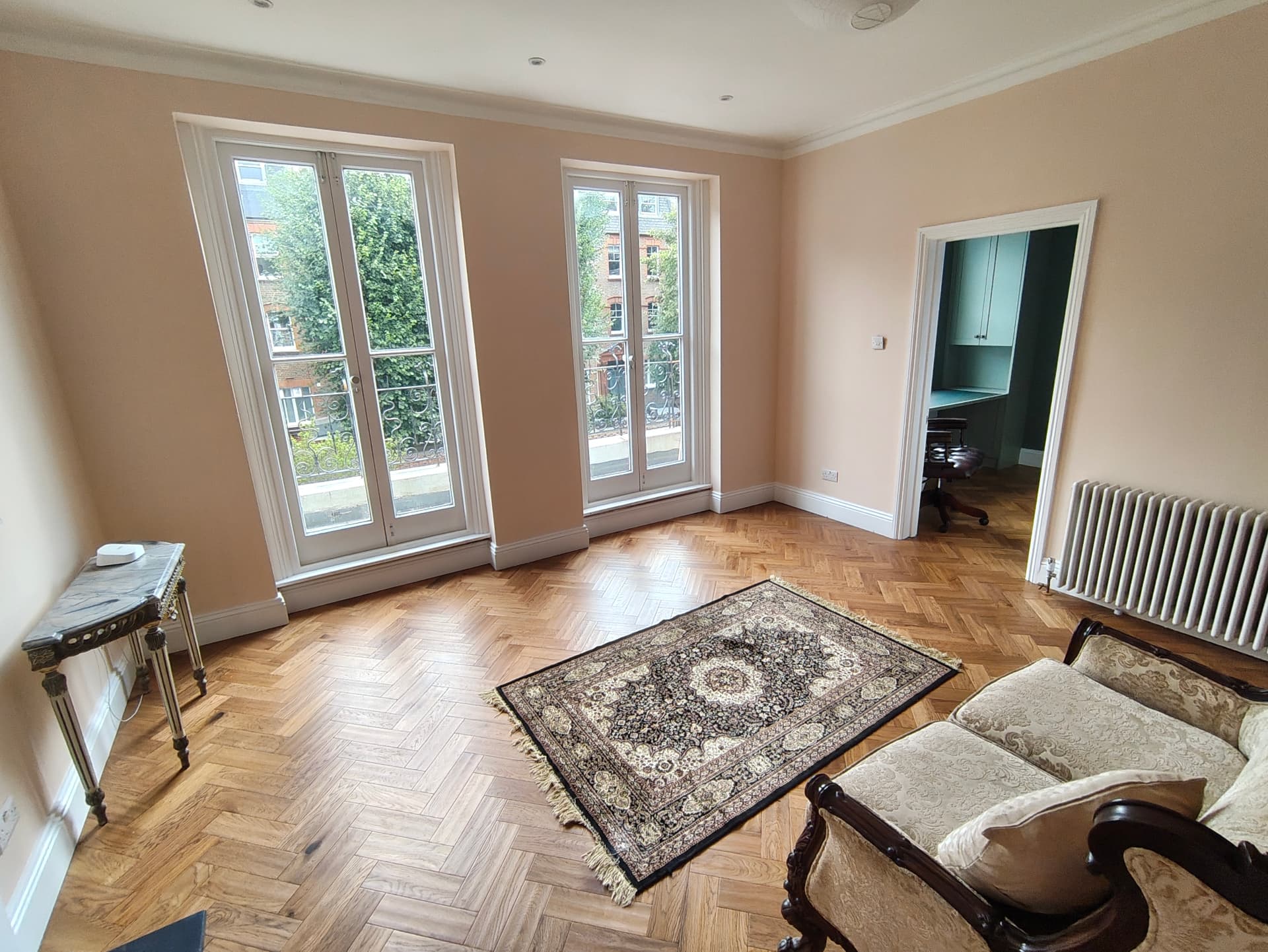 Double-aspect drawing room with tall French windows, herringbone parquet flooring and restored cornicing