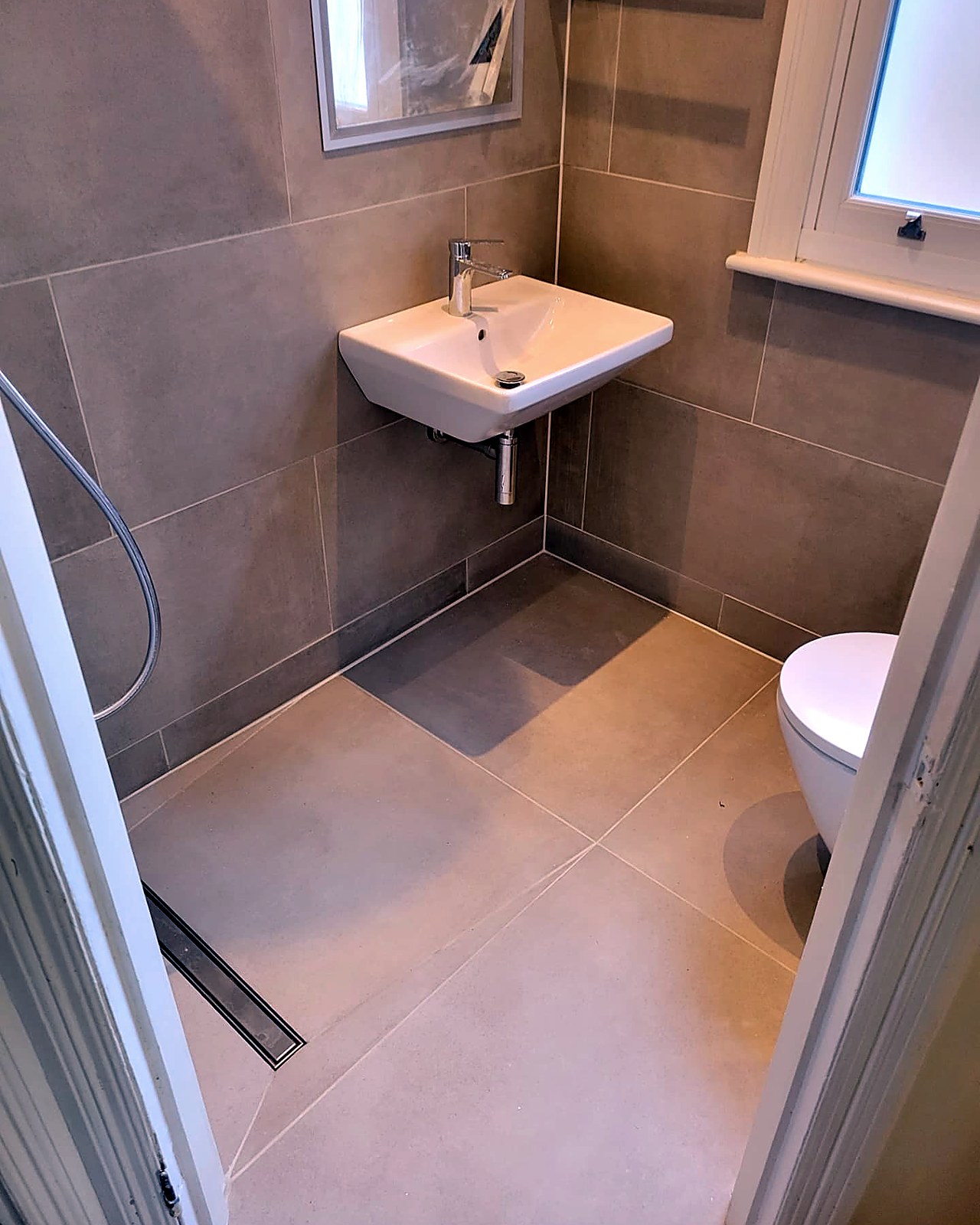 Completed level-access wet room in South Tottenham with porcelain tiling, wall-hung basin and concealed cistern WC