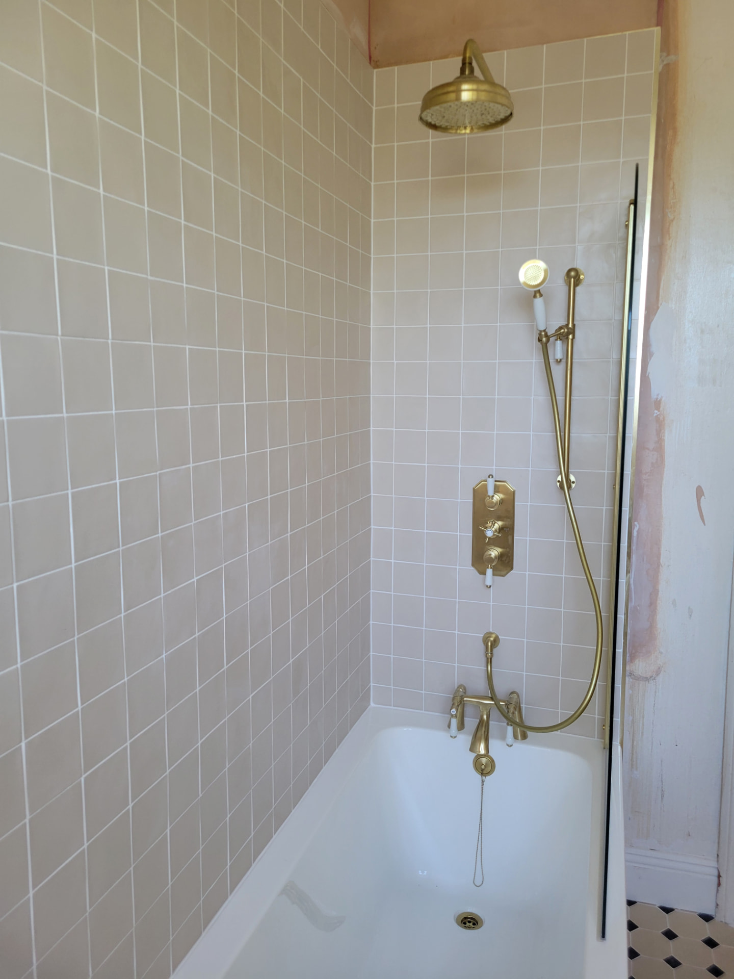 Brass shower fittings and pale wall tiles above the bath
