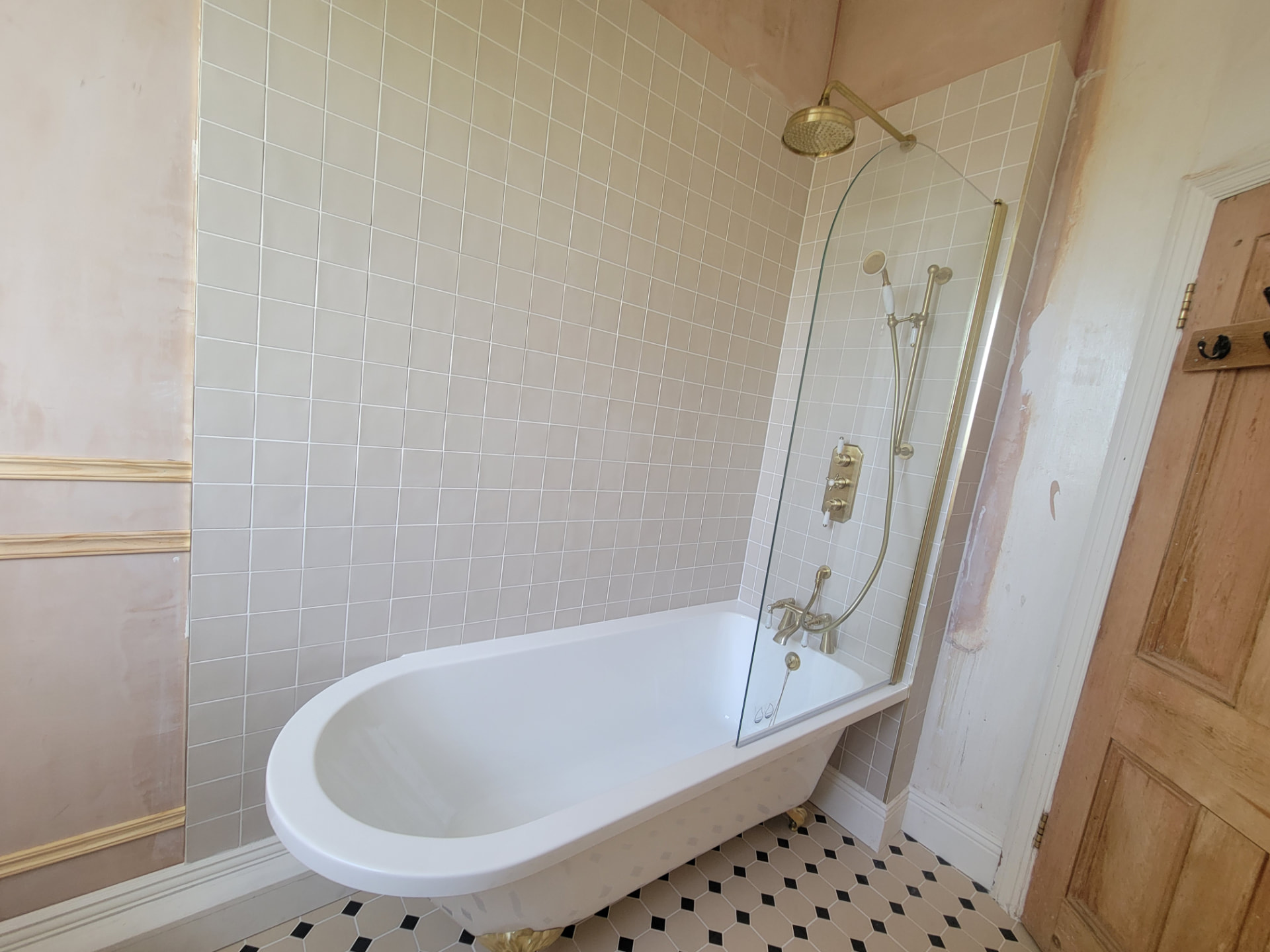 Bath and shower beneath the brass fittings and tiled wall