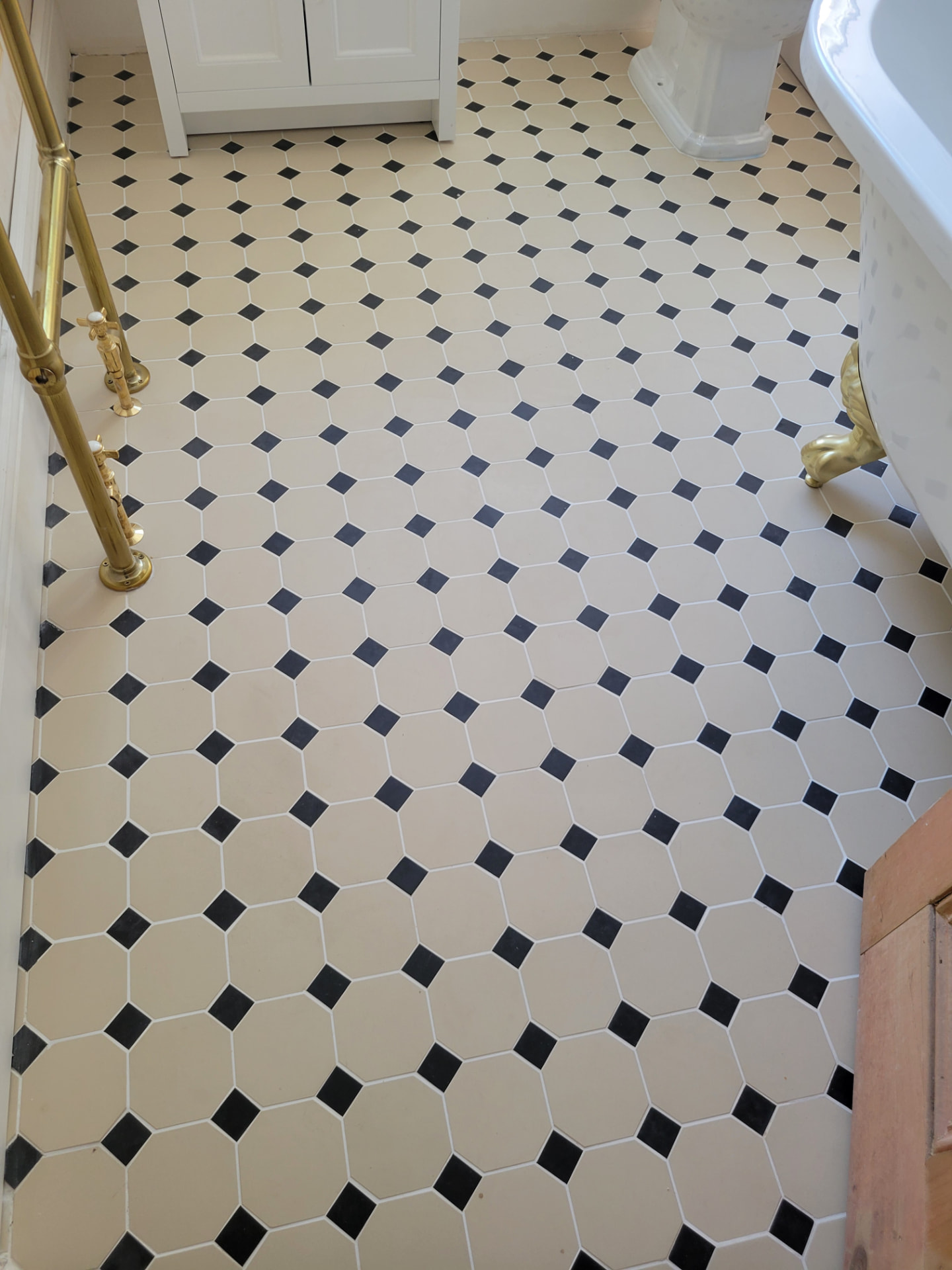 Pale cream floor tiles with small black diamond inserts beside the bath